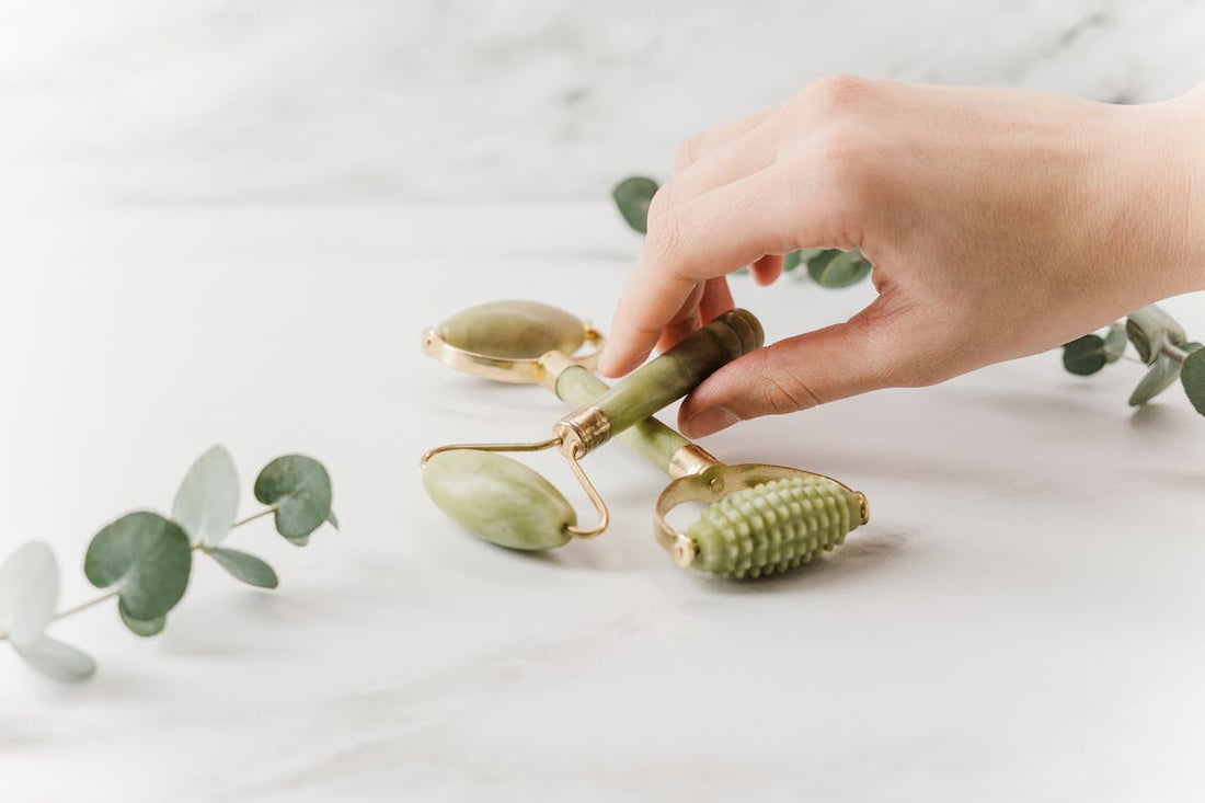 Person holding green skincare tools and leaves on white textile